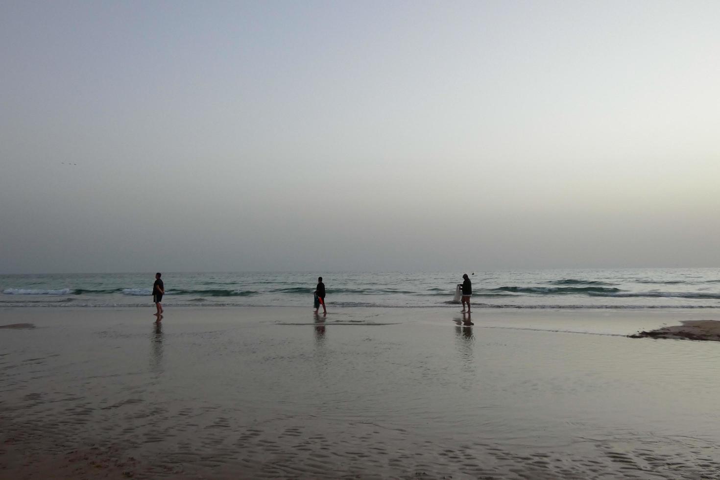 playa solitaria con gente paseando por la arena al borde de las olas del mar foto