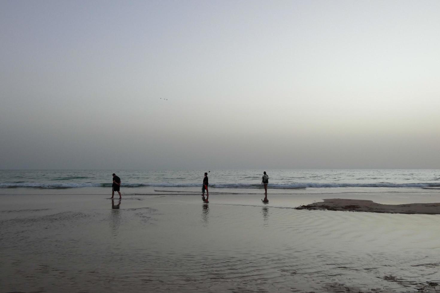 playa solitaria con gente paseando por la arena al borde de las olas del mar foto