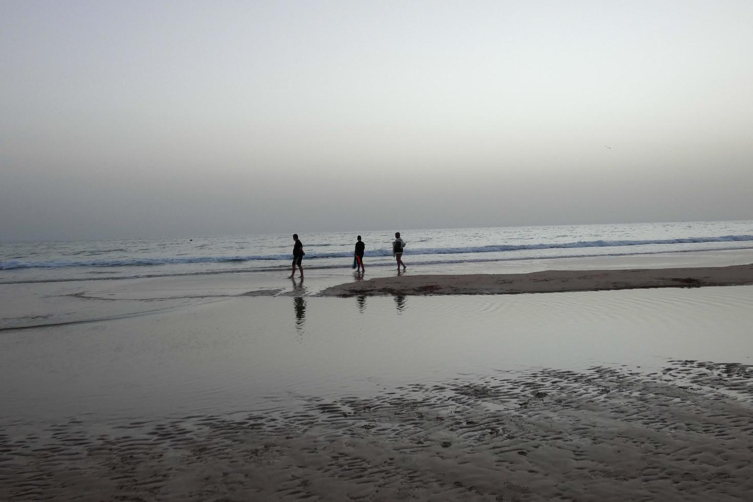 lonely beach with people strolling on the sand at the edge of the sea waves photo