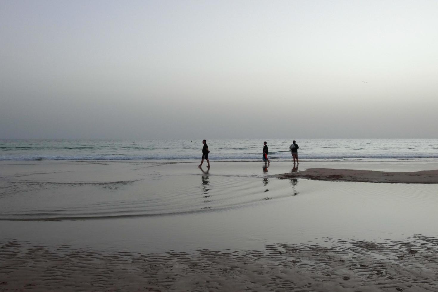 playa solitaria con gente paseando por la arena al borde de las olas del mar foto