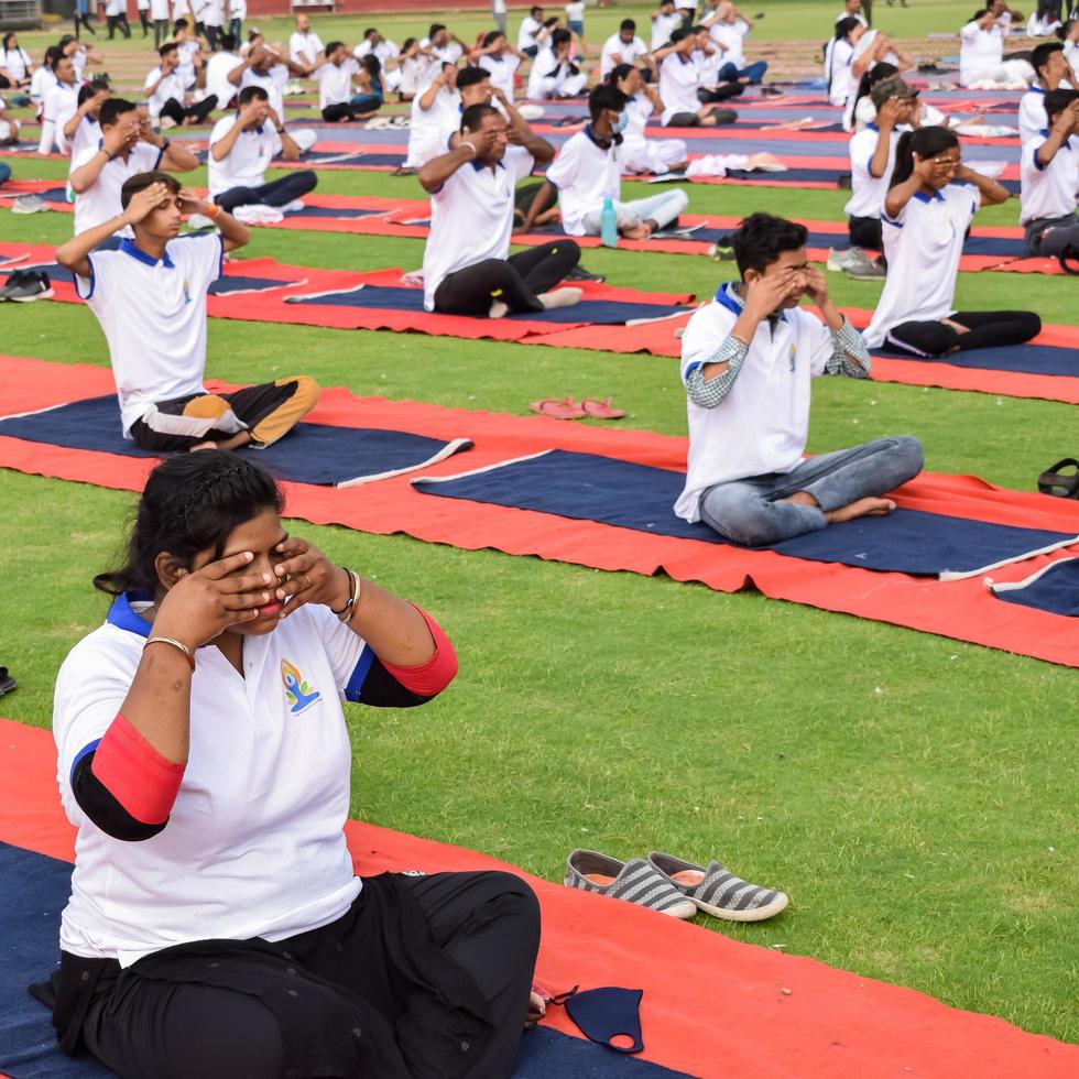 New Delhi, India, June 21 2022 - Group Yoga exercise session for people at Yamuna Sports Complex in Delhi on International Yoga Day, Big group of adults attending yoga class in cricket stadium photo