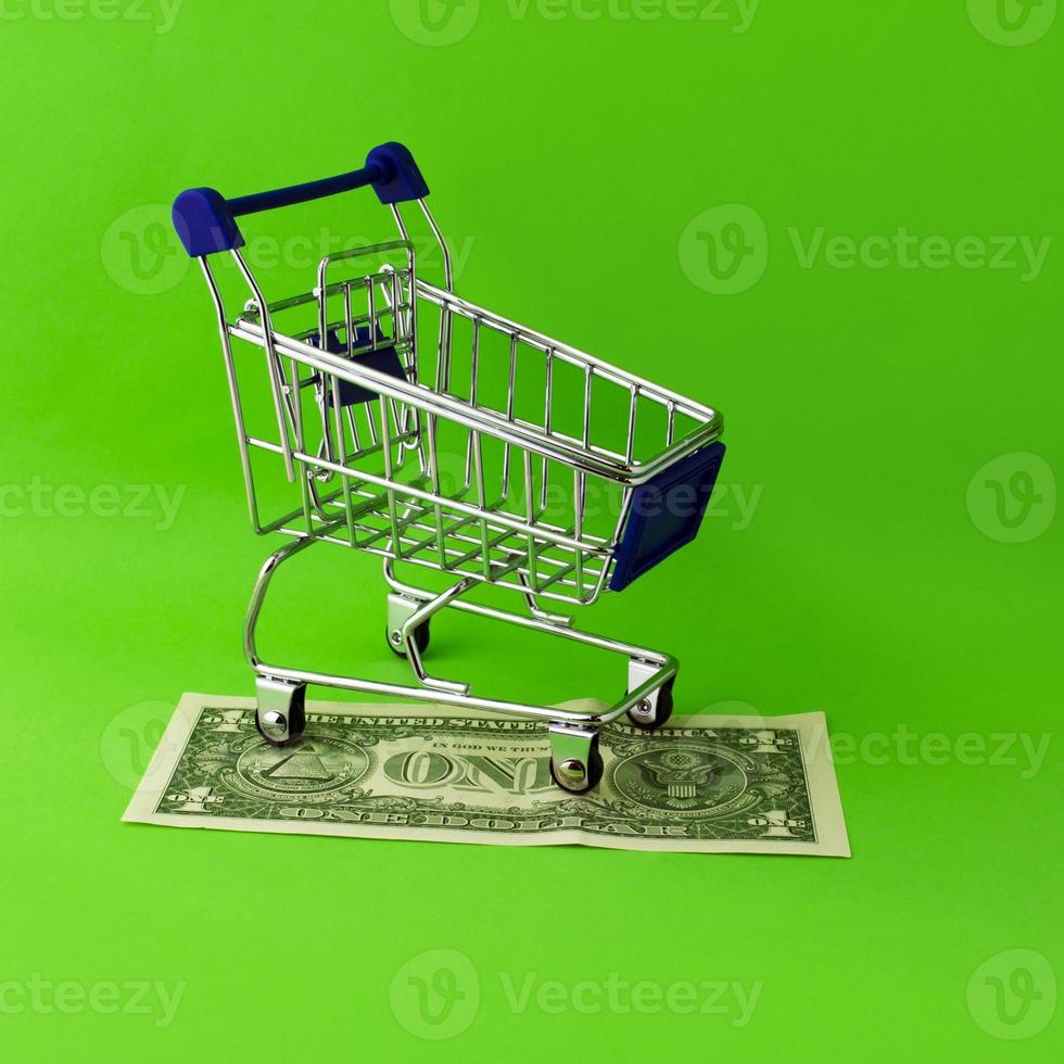 A shopping cart stands on a 1 dollar bill on a green background. photo