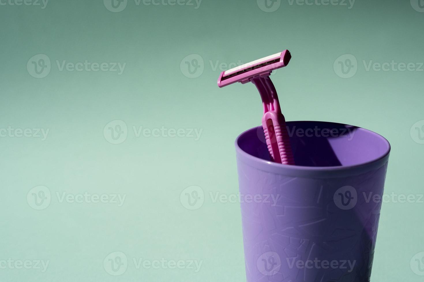 Disposable razor in a purple glass, a creative composition of a disposable razor on a turquoise background photo