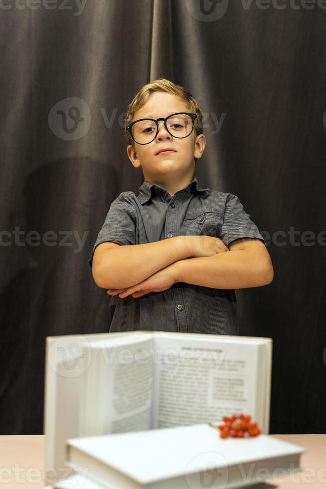 a boy with glasses folded his arms on his chest, a serious look, a stack of books, back to school photo