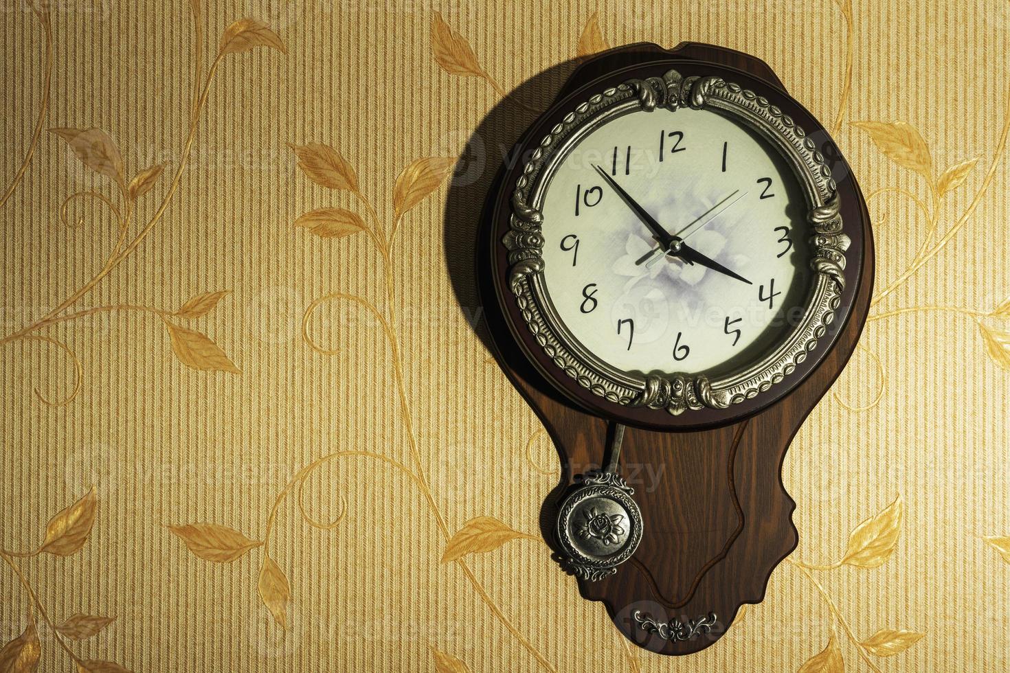 Round home brown wall Clock with a pendulum on a light wall photo