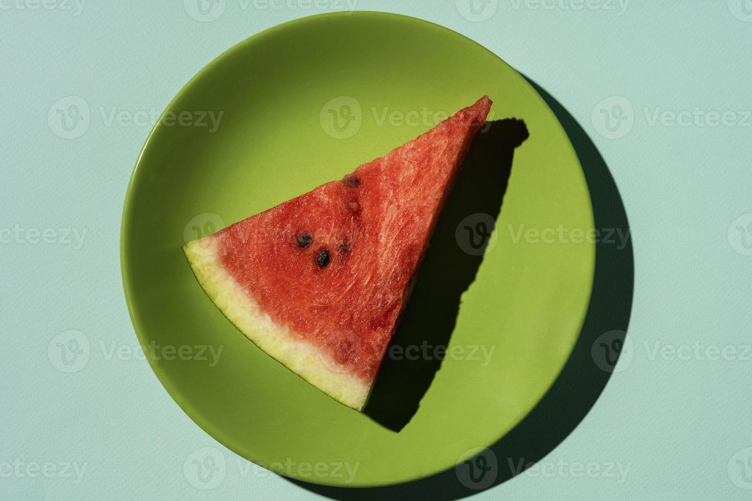 rebanada de sandía en un plato verde sobre un fondo turquesa, vista superior foto