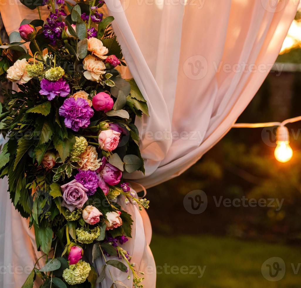 Wedding twilight ceremony decoration made of hanging on a tree golden lanterns and lamps and standing on the grass fired candles with the carpet in the middle photo