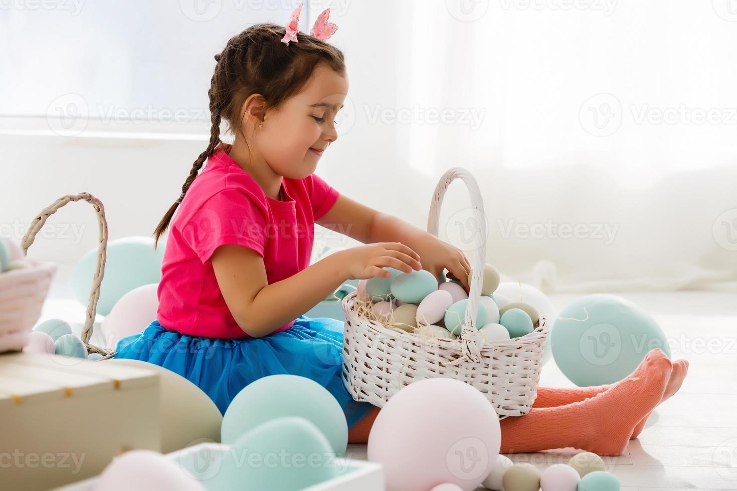 Getting ready to Easter. Lovely little girl holding an Easter egg and smiling with decoration in the background photo