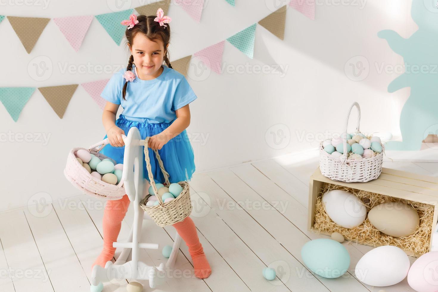 Getting ready to Easter. Lovely little girl holding an Easter egg and smiling with decoration in the background photo