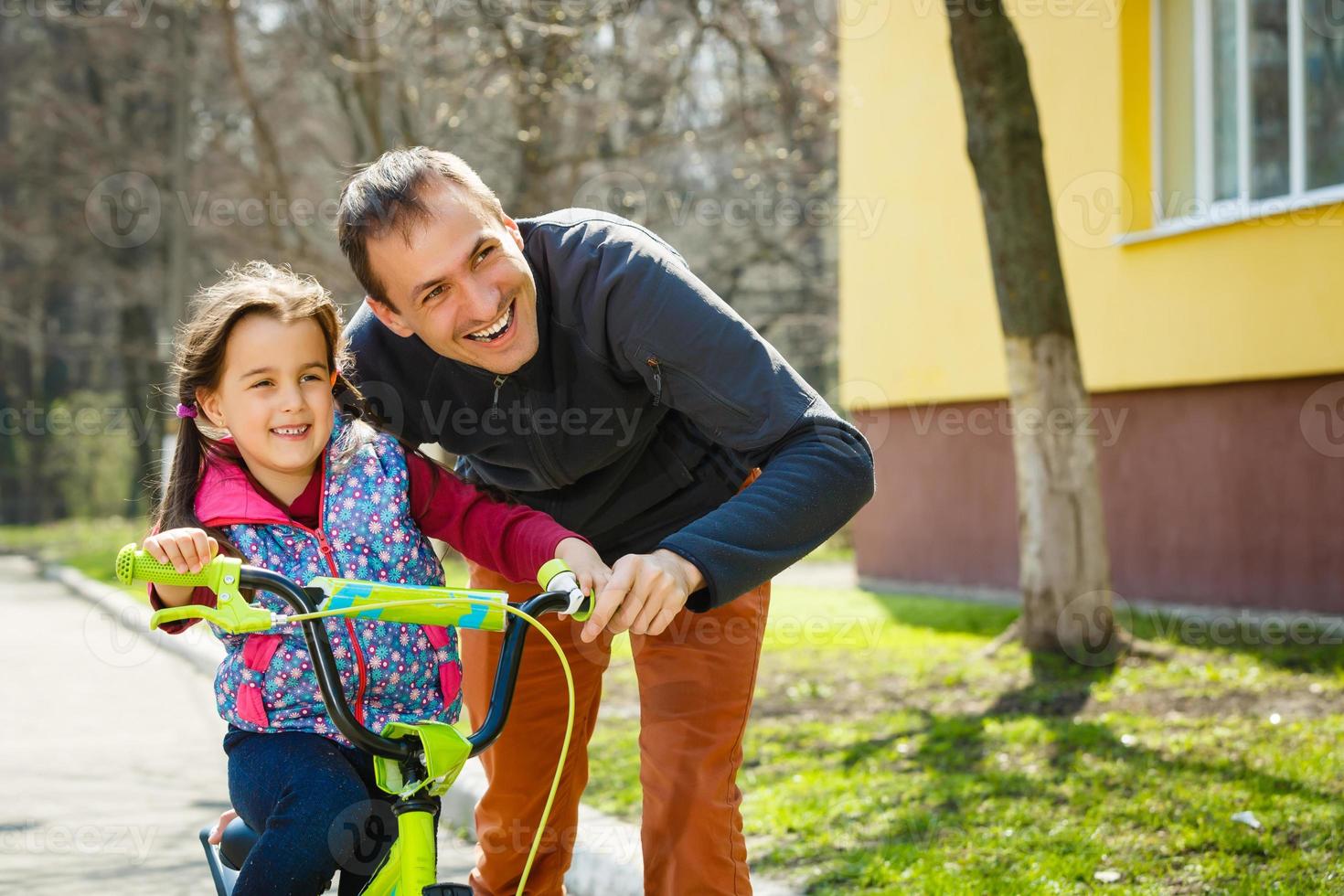 padre feliz enseñando a su pequeña hija a andar en bicicleta. niño aprendiendo a andar en bicicleta. actividades familiares en verano. foto