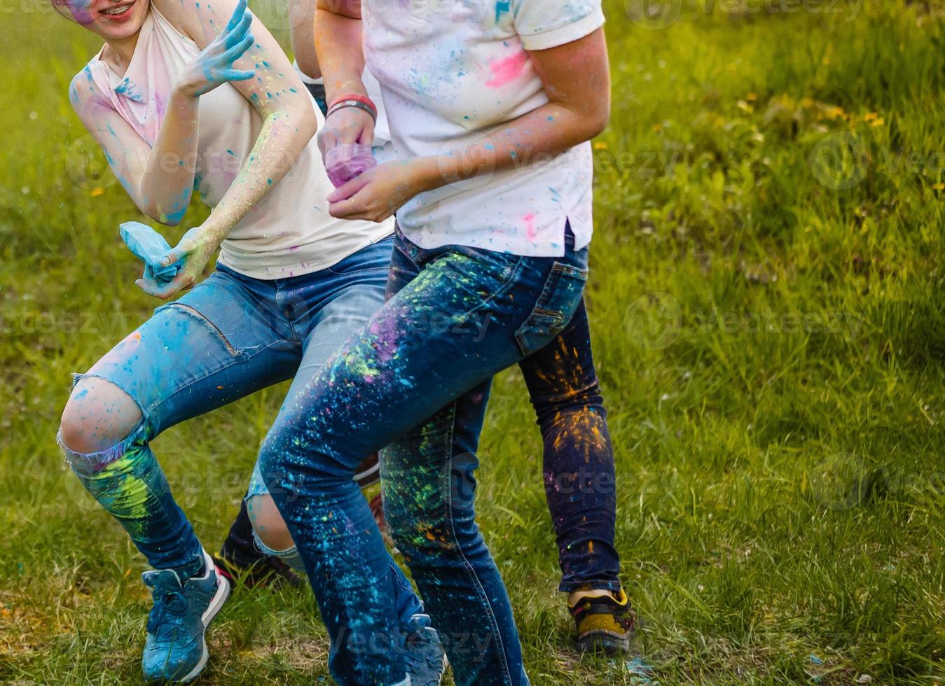 Cheerful young multiethnic friends with colorful paint on clothes and bodies having fun together at holi festival photo