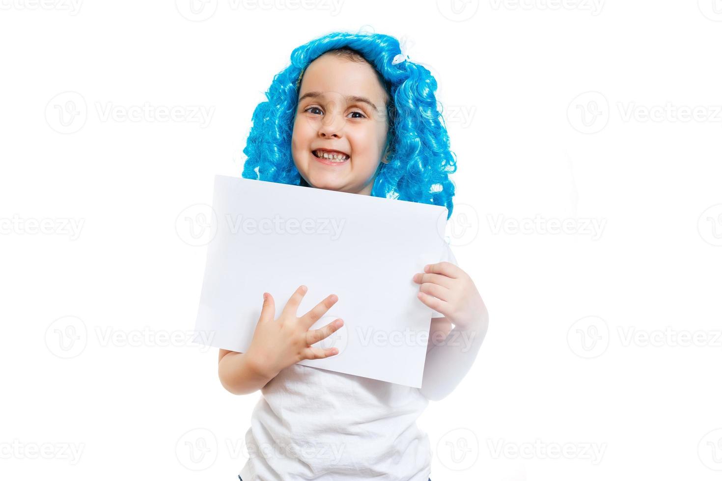 Young little girl in blue wig holding white blank sheet of paper isolated on white photo