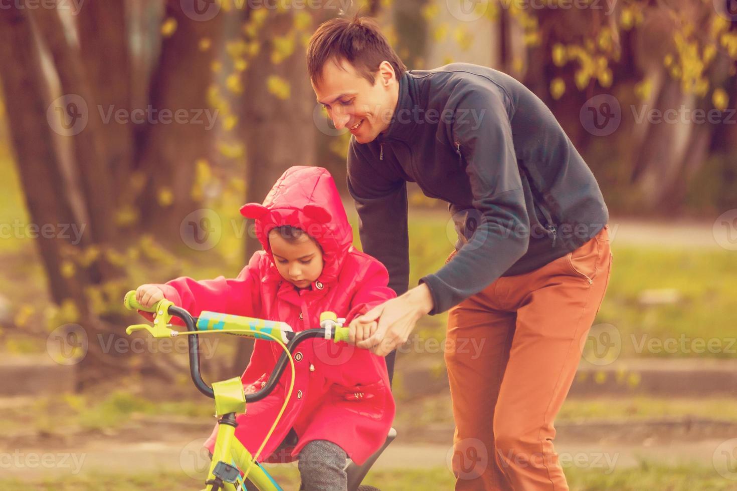 Happy father teaching his little daughter to ride a bicycle. Child learning to ride a bike. Family activities at summer photo