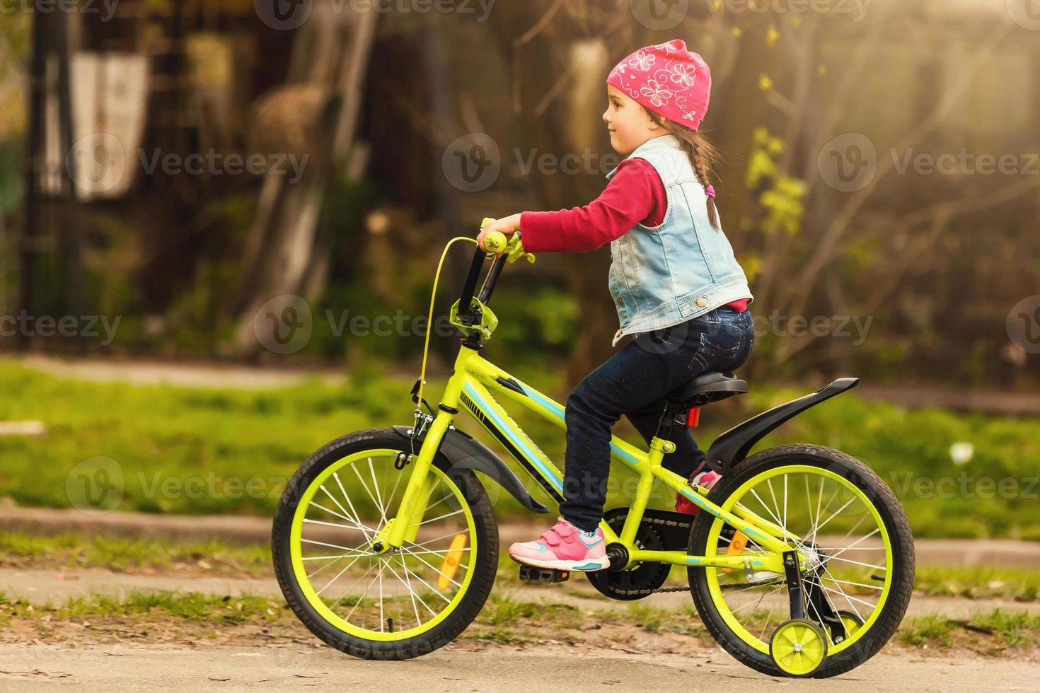 Beautiful smiling little girl riding bicycle in a park photo