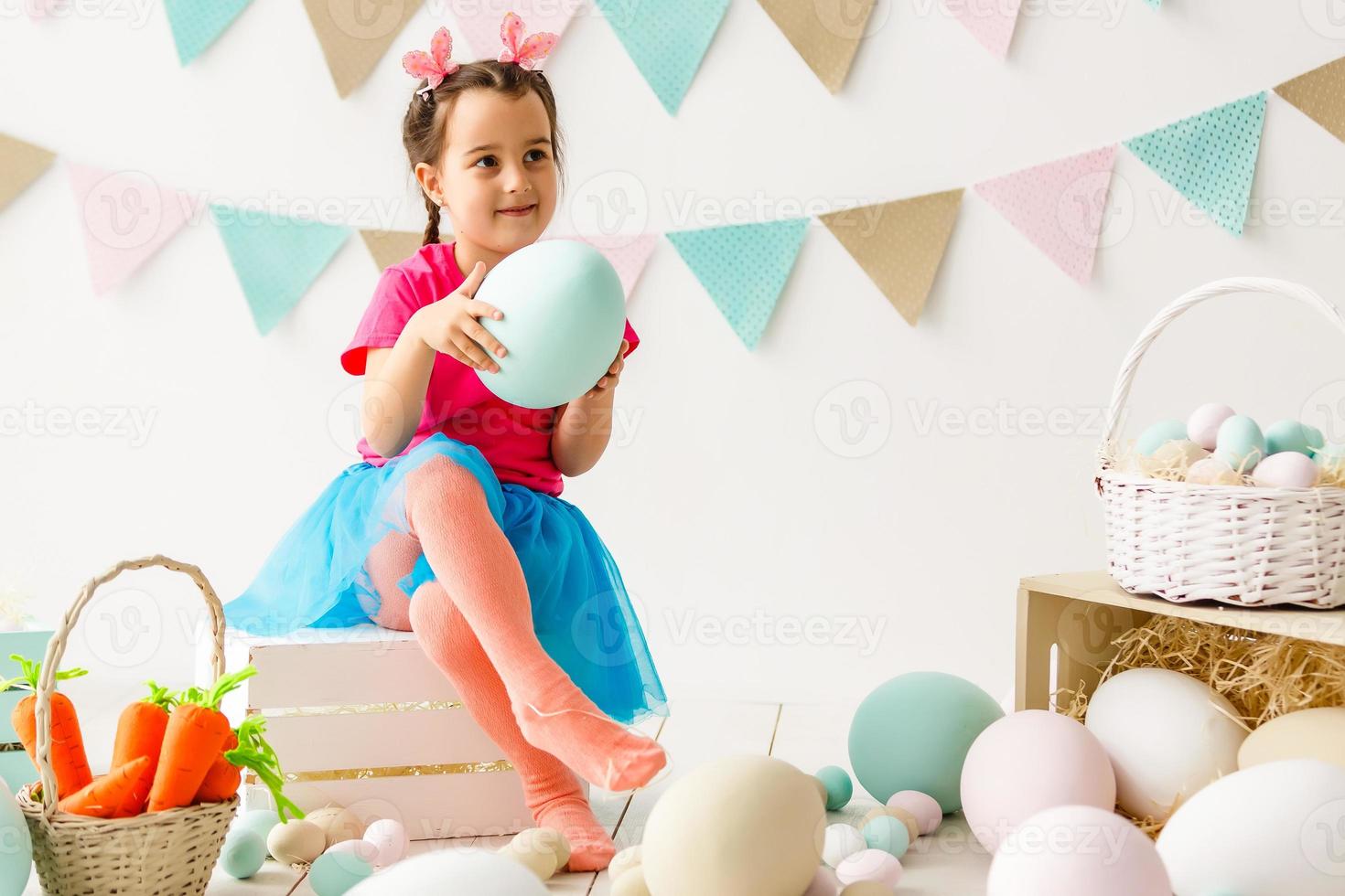 Getting ready to Easter. Lovely little girl holding an Easter egg and smiling with decoration in the background photo