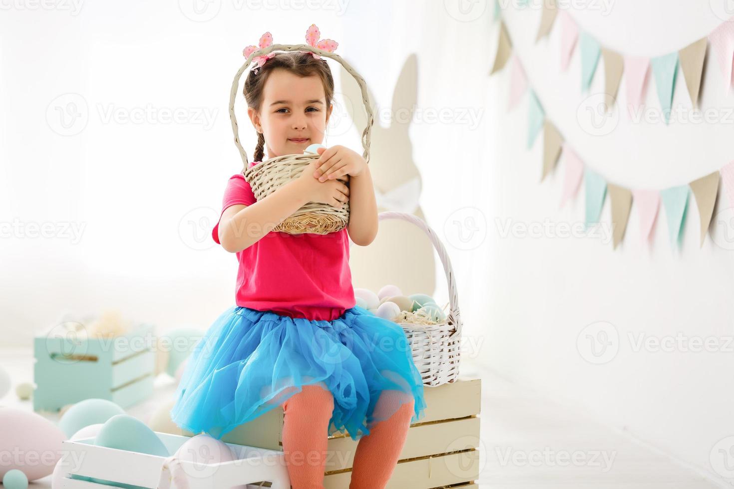 Getting ready to Easter. Lovely little girl holding an Easter egg and smiling with decoration in the background photo