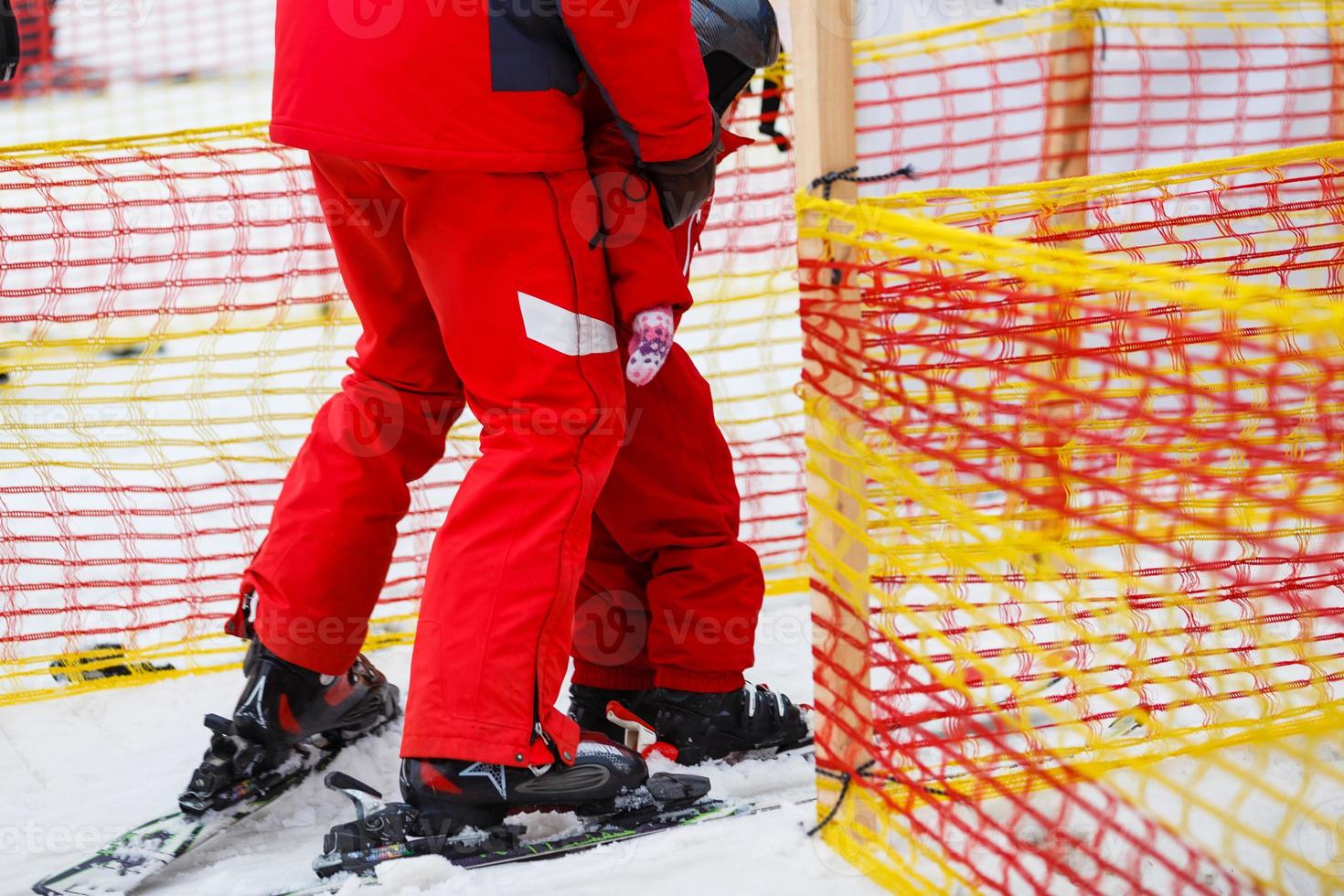 Little girl in red learning to ski with the help of an adult photo