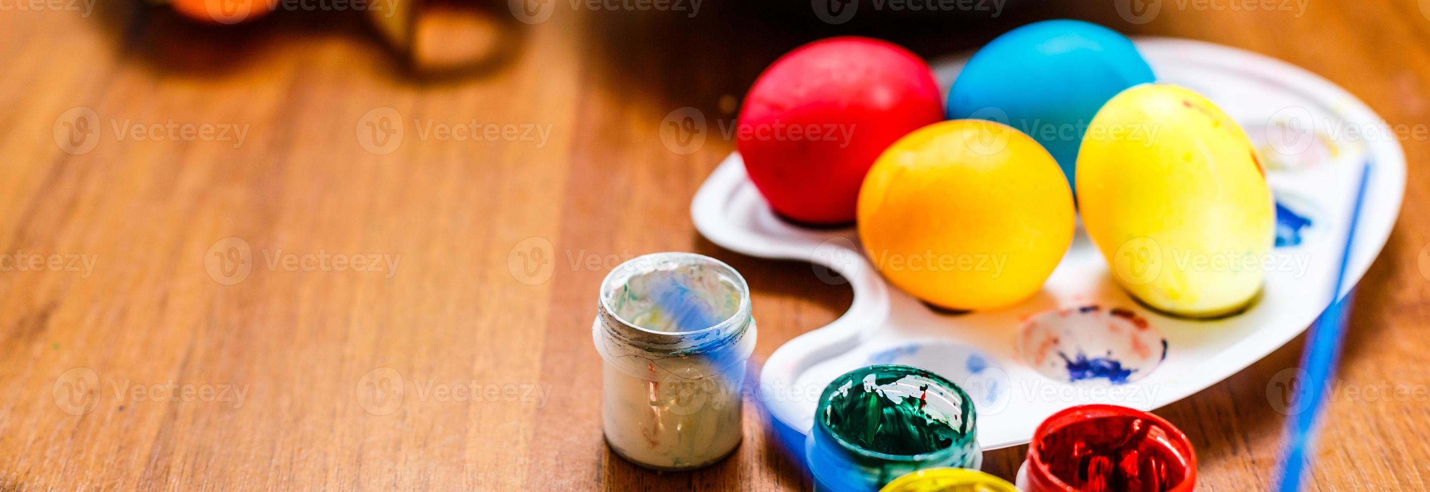 Multicolored easter painted handmade eggs, paints and brushes. Festive Easter frame from eggs, paints and brushes on white wooden background with space for text photo