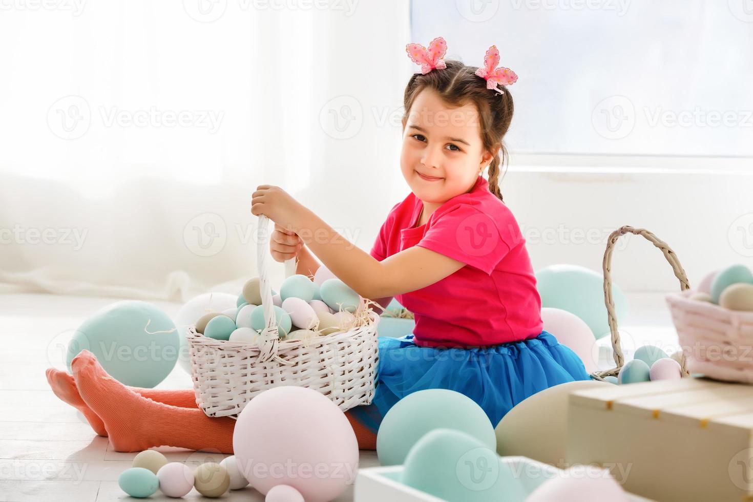 Getting ready to Easter. Lovely little girl holding an Easter egg and smiling with decoration in the background photo