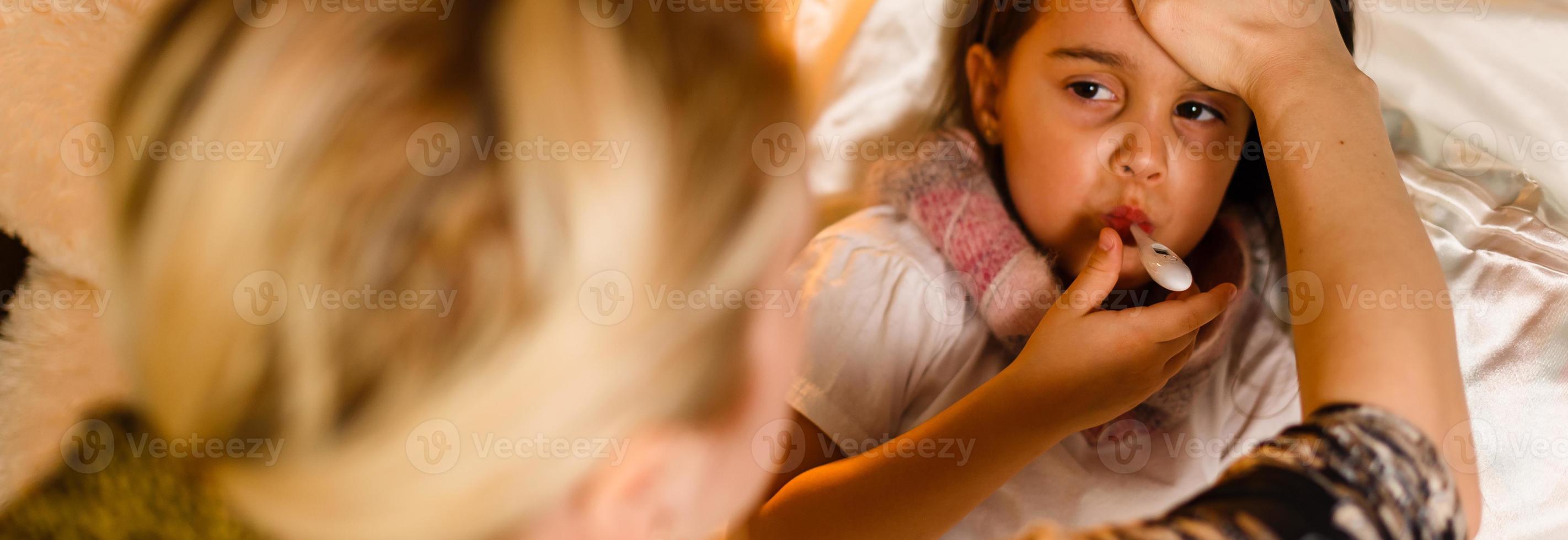 Mother measuring temperature of her ill kid by hand. Sick child with high fever laying in bed and mother holding thermometer, Healthy care concept photo