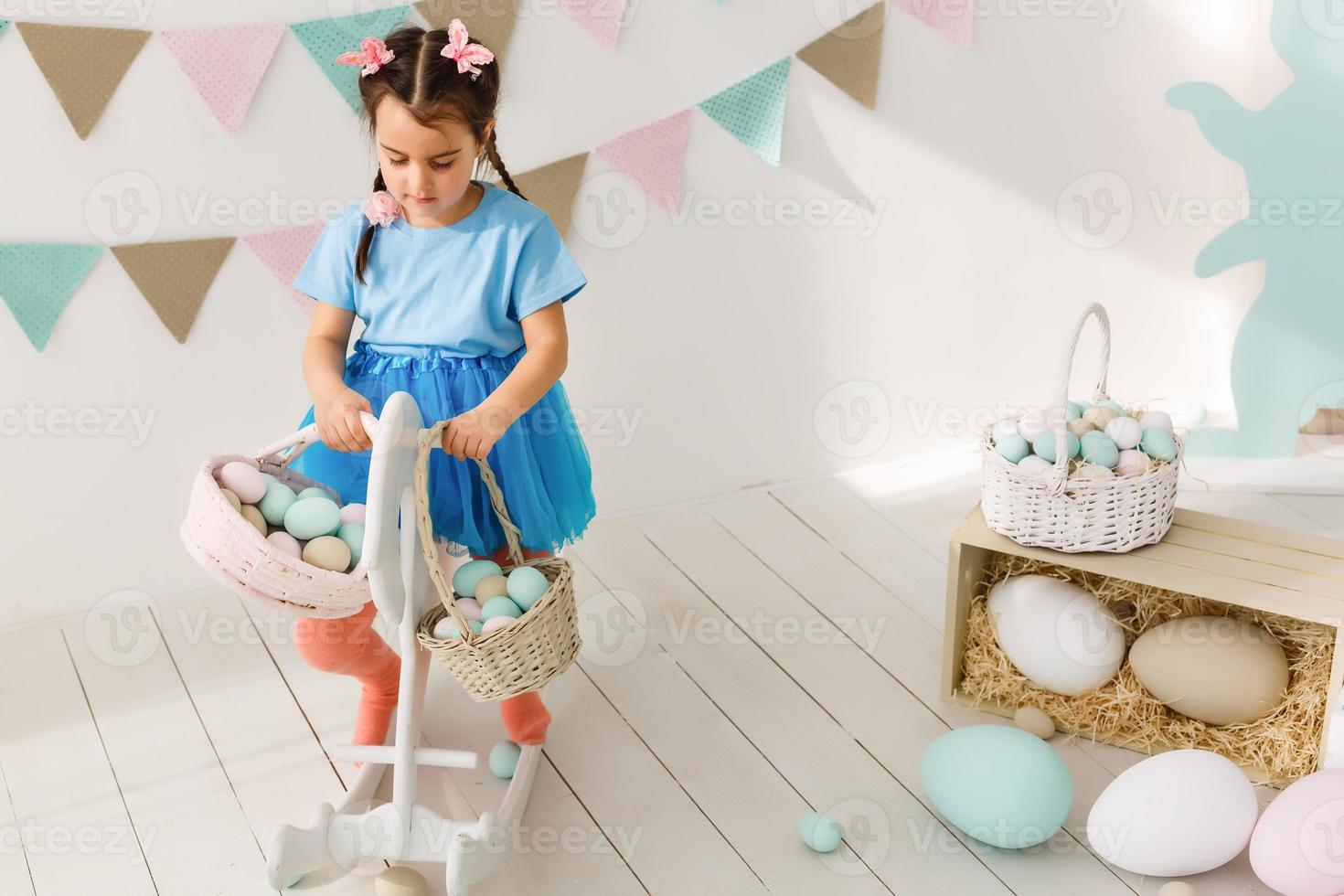 Getting ready to Easter. Lovely little girl holding an Easter egg and smiling with decoration in the background photo