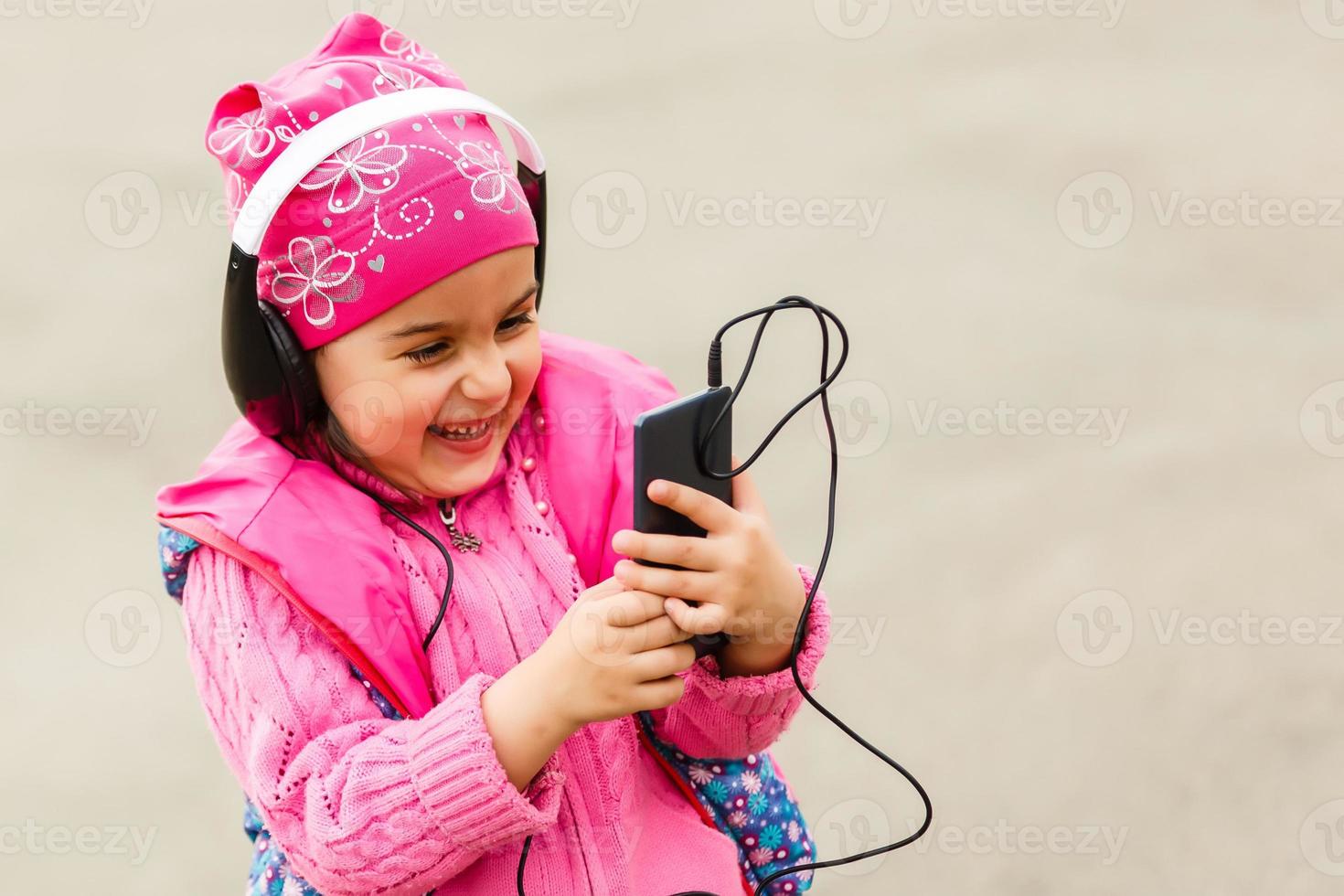 Little beautiful girl enjoys the phone. She headphones. Kids and Technology photo