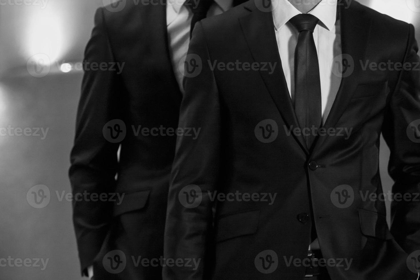 Portrait of two sexy handsome fashion male models men dressed in elegant suits on black studio photo