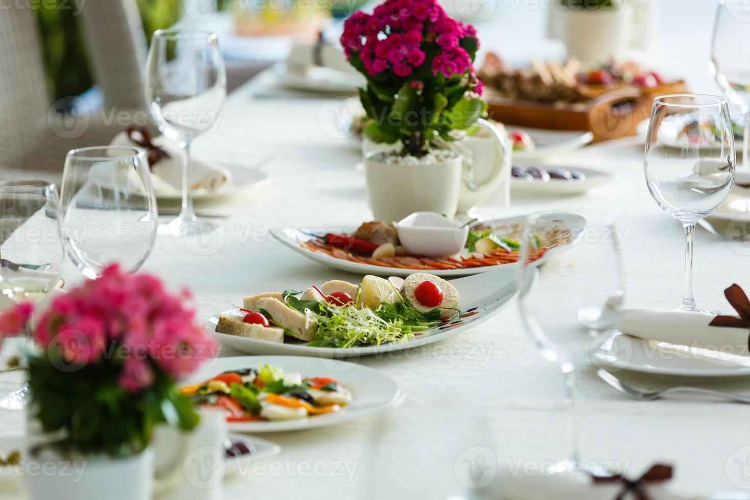 Table served for special occasion. Empty plate, glasses, forks, napkin and flowers on table covered with white tableclothes. Elegant dinner table. White table setting photo
