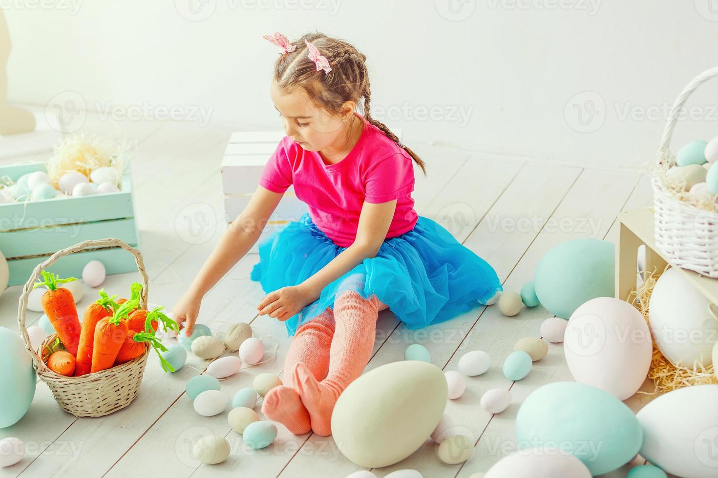 Cute little child girl wearing bunny ears on Easter day. Girl sitting with a basket of Easter eggs. Child girl laughs and enjoys spring and a holiday. photo