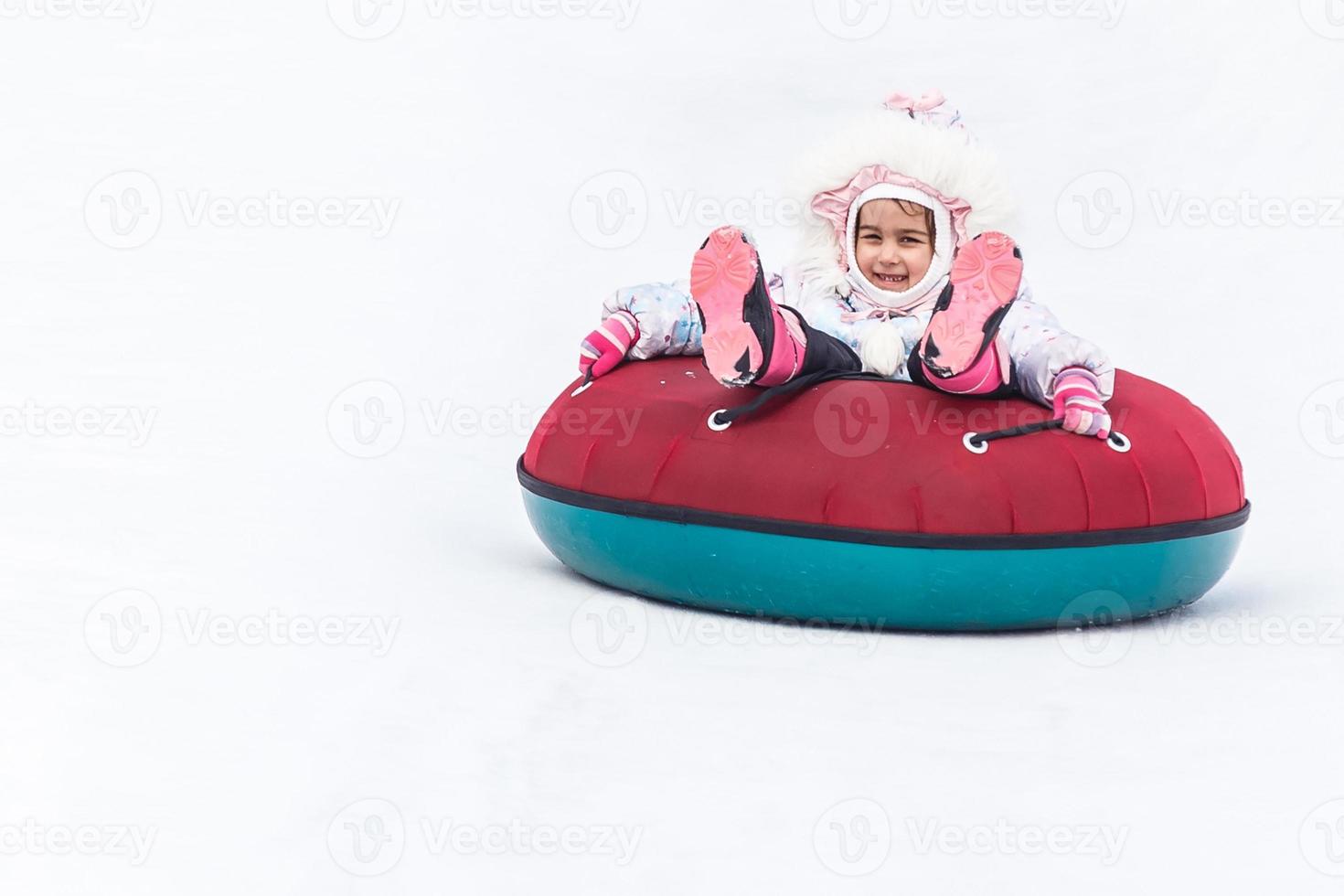 Little girl with snowtube ready for sledding down a hill photo