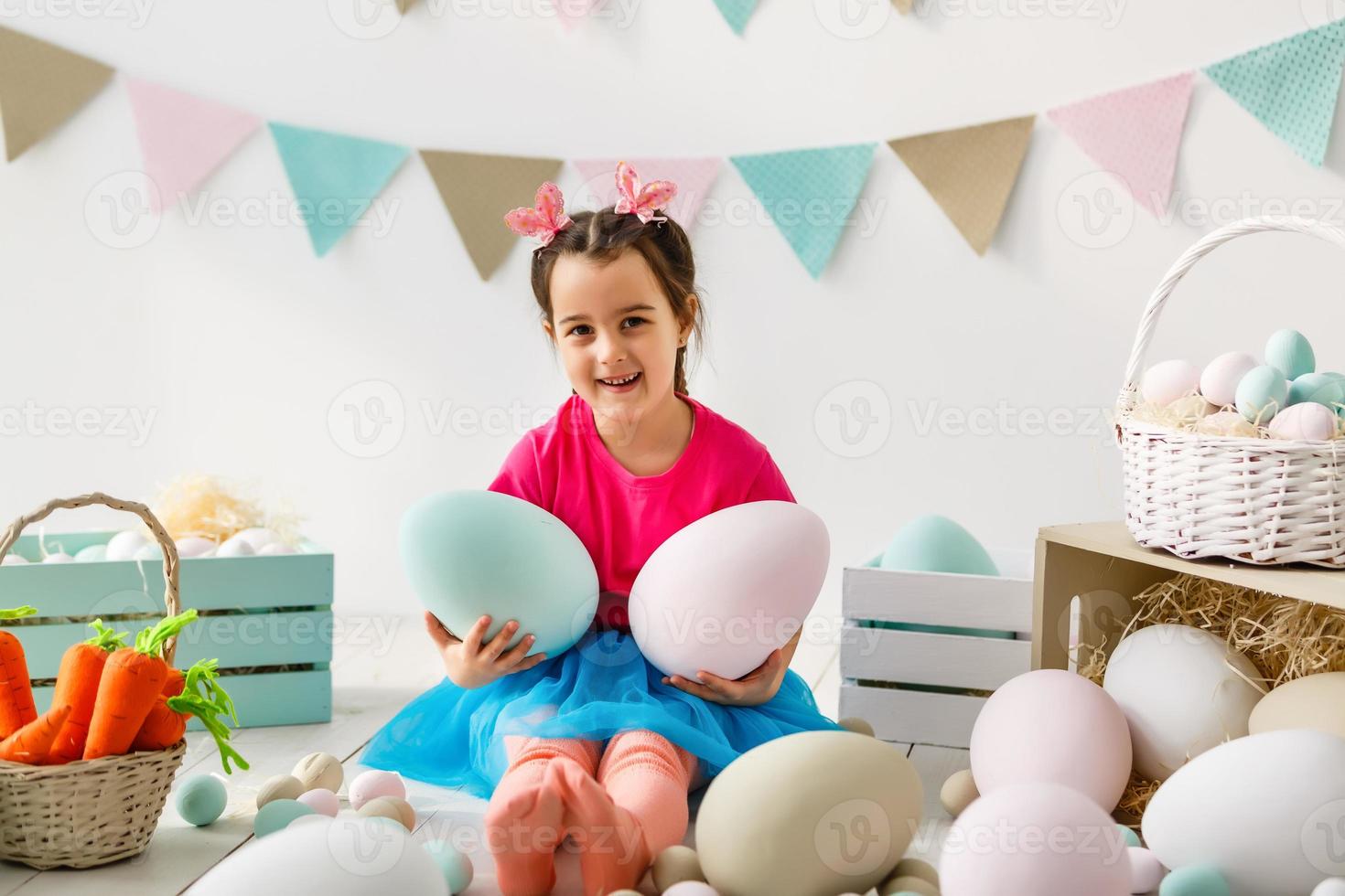 Getting ready to Easter. Lovely little girl holding an Easter egg and smiling with decoration in the background photo