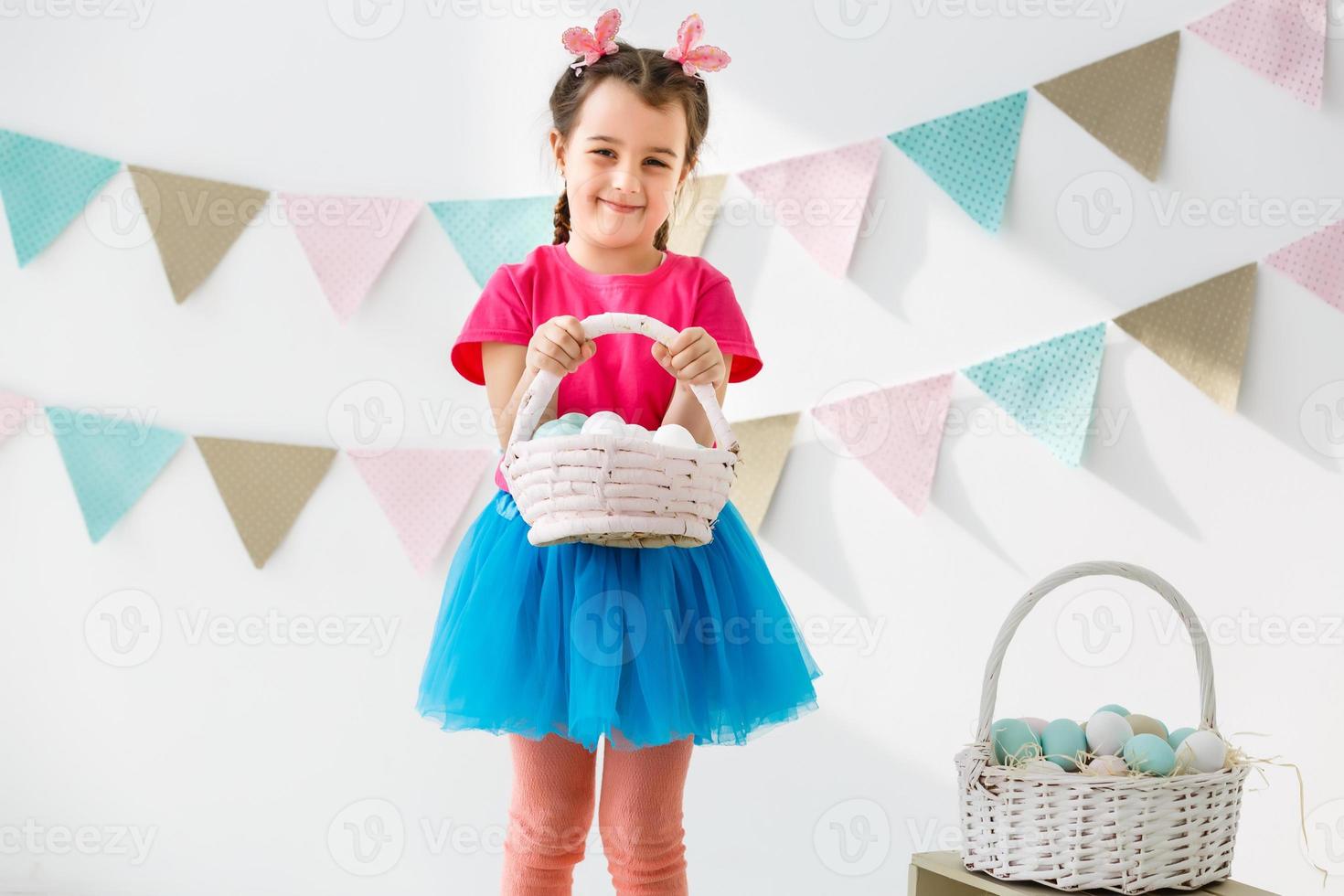 Getting ready to Easter. Lovely little girl holding an Easter egg and smiling with decoration in the background photo