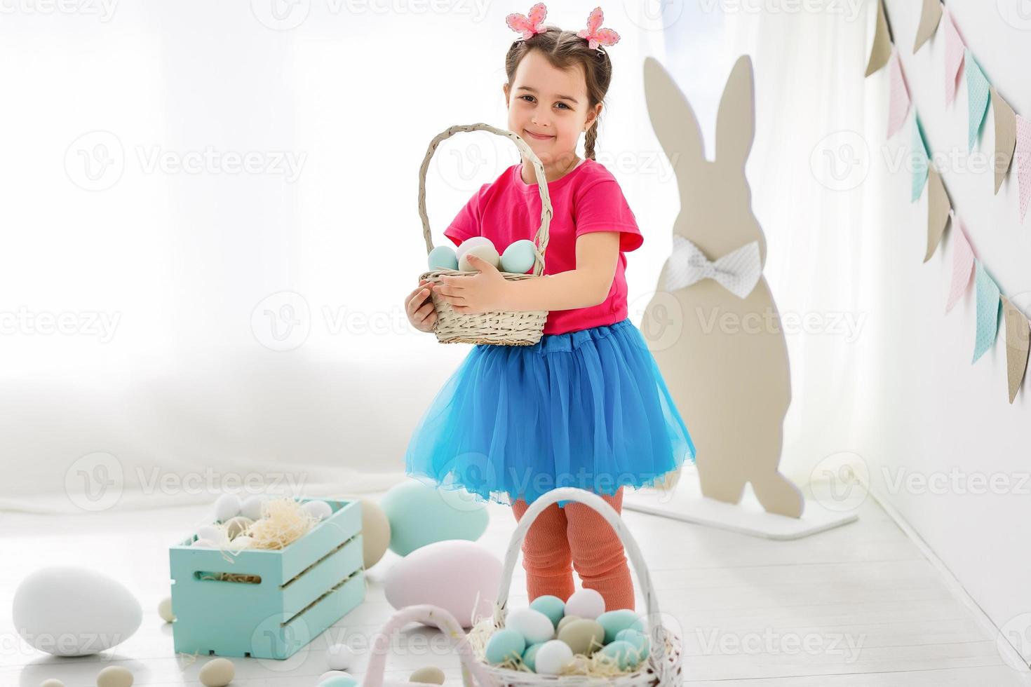 Getting ready to Easter. Lovely little girl holding an Easter egg and smiling with decoration in the background photo