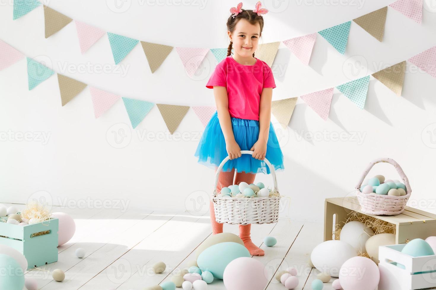 Getting ready to Easter. Lovely little girl holding an Easter egg and smiling with decoration in the background photo