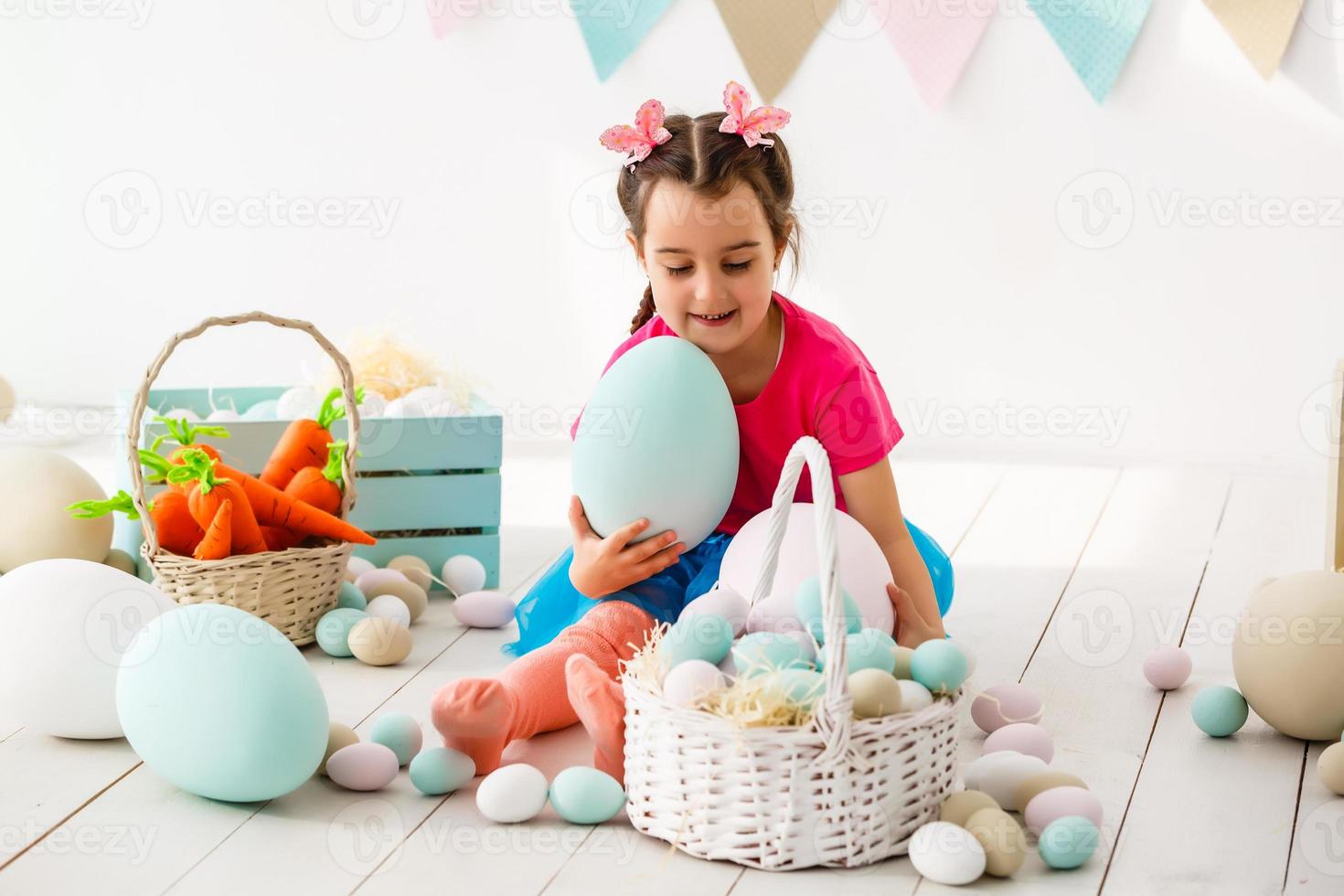 Getting ready to Easter. Lovely little girl holding an Easter egg and smiling with decoration in the background photo