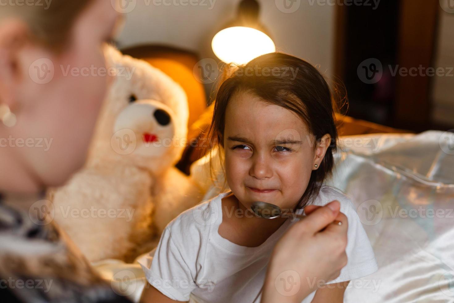 Sick little girl in bed taking medicine with spoon photo