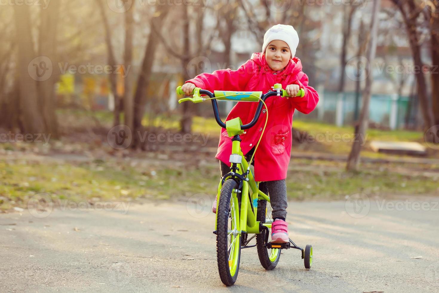 Little girl in red riding a bicycle outdoors photo