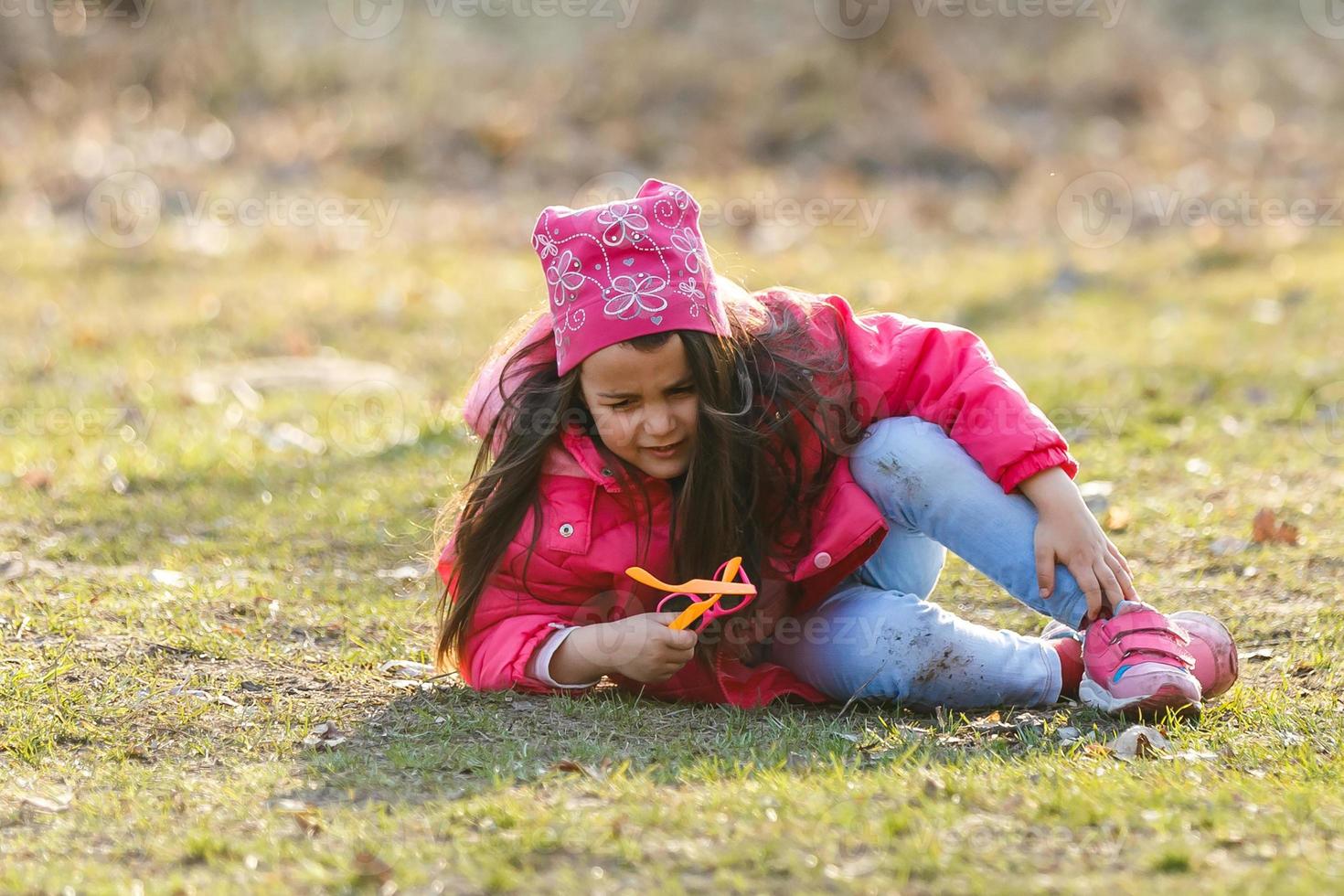 A little girl is crying loudly in the spring forest. She sits on the grass and fallen leaves. She opens her mouth wide and screams. On the face emotions of despair and resentment photo