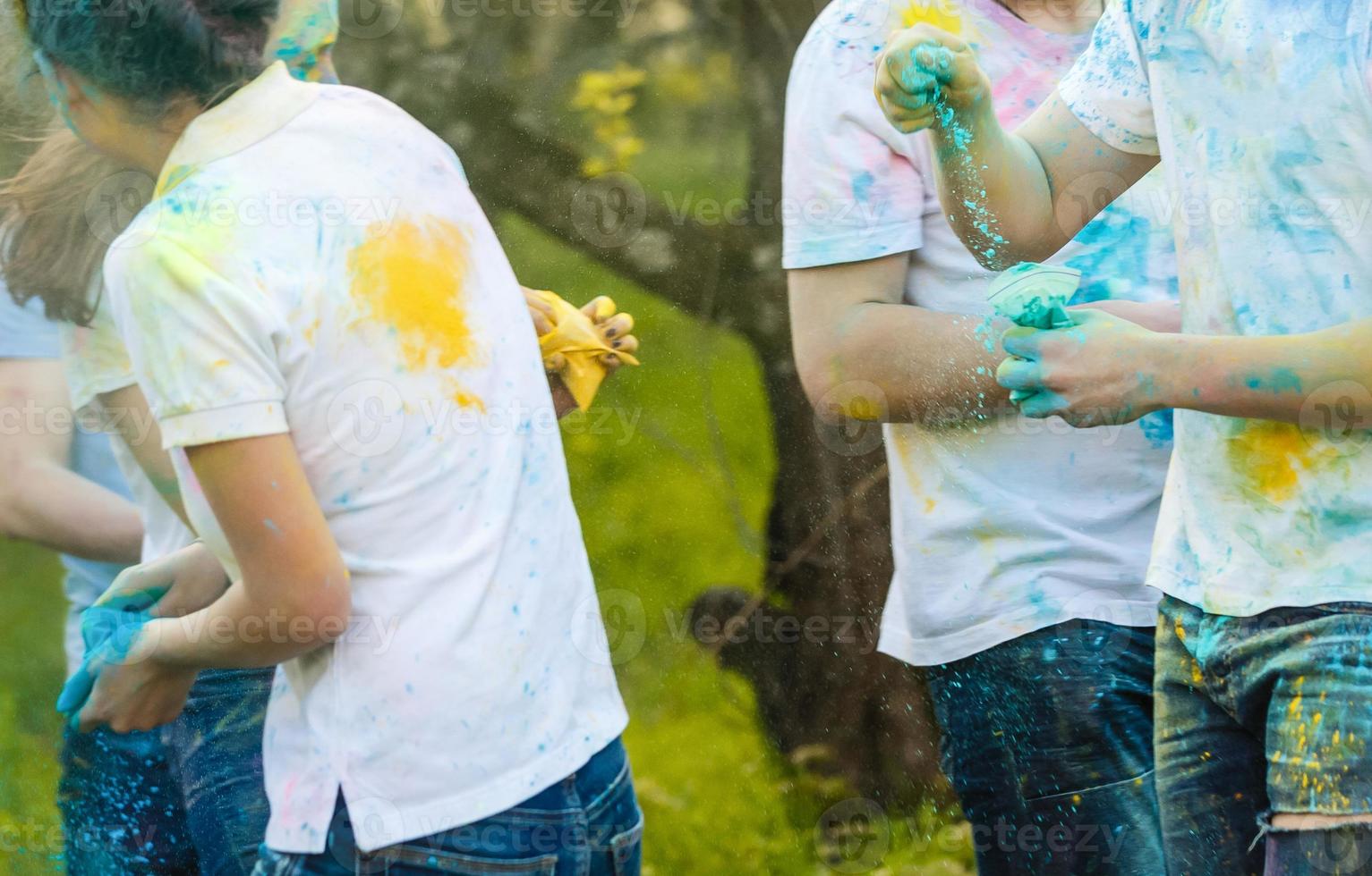 Cheerful young multiethnic friends holding colorful paint in hands at holi festival photo