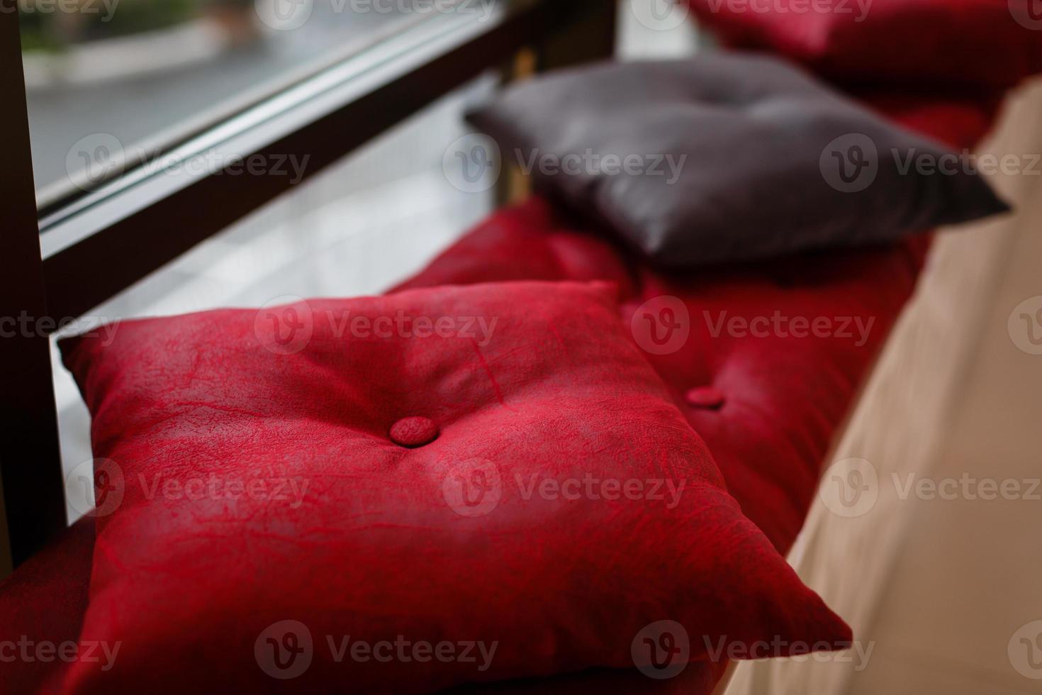 Red cushions lying strewn on a sunbed with low light coming in through the venetian blinds photo