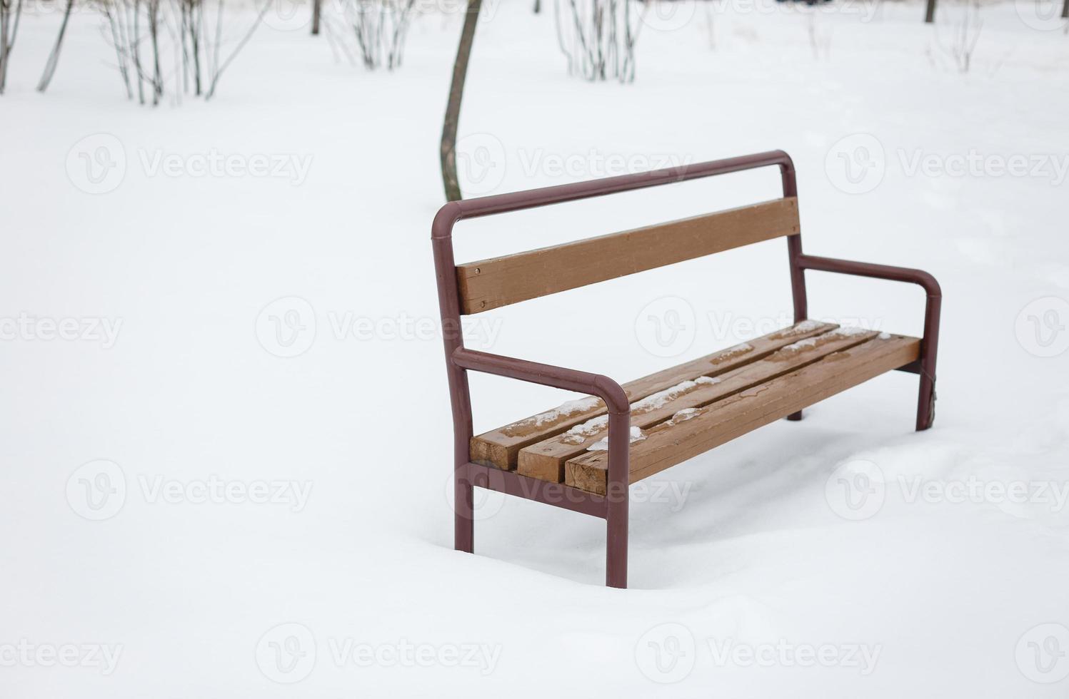 taller de hierro, negro con un asiento de madera, se encuentra en un parque de invierno, en la nieve foto