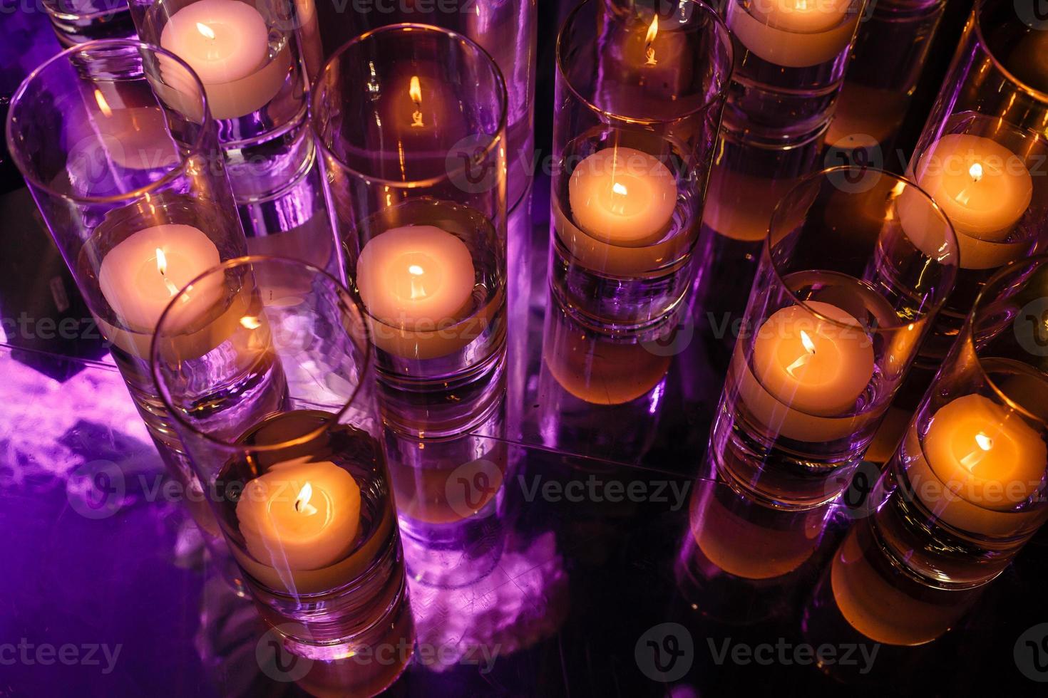 primer plano de velas candelita ardiendo en vasos de chupito. el foco está en el cristal derecho, con poca profundidad de campo. imagen con poca luz ambiental. foto