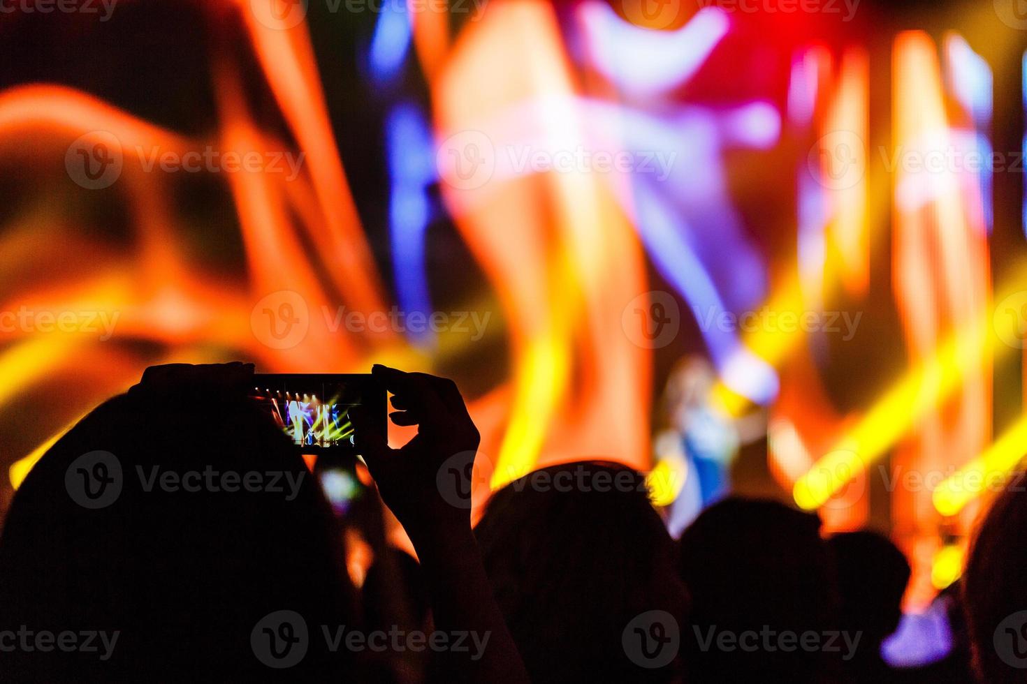 un teléfono inteligente sostenido con dos manos para filmar un metraje durante un concierto. foto