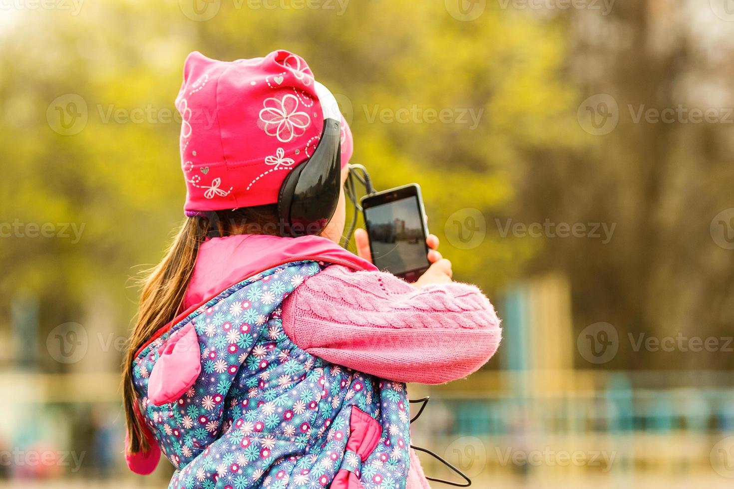 colegiala niña. verano en la naturaleza. en manos sosteniendo un teléfono inteligente escuchando música en los auriculares. toma una foto por teléfono, hablando en la videollamada. la emoción sonríe alegremente.