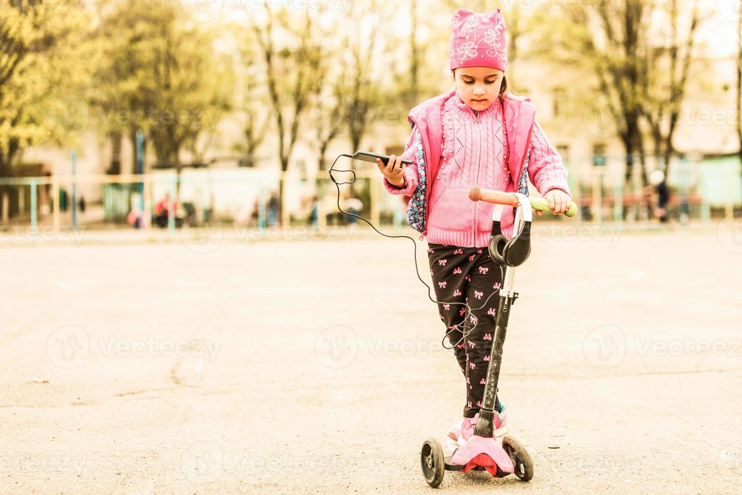 Little beautiful girl enjoys the phone. She headphones. Kids and Technology photo