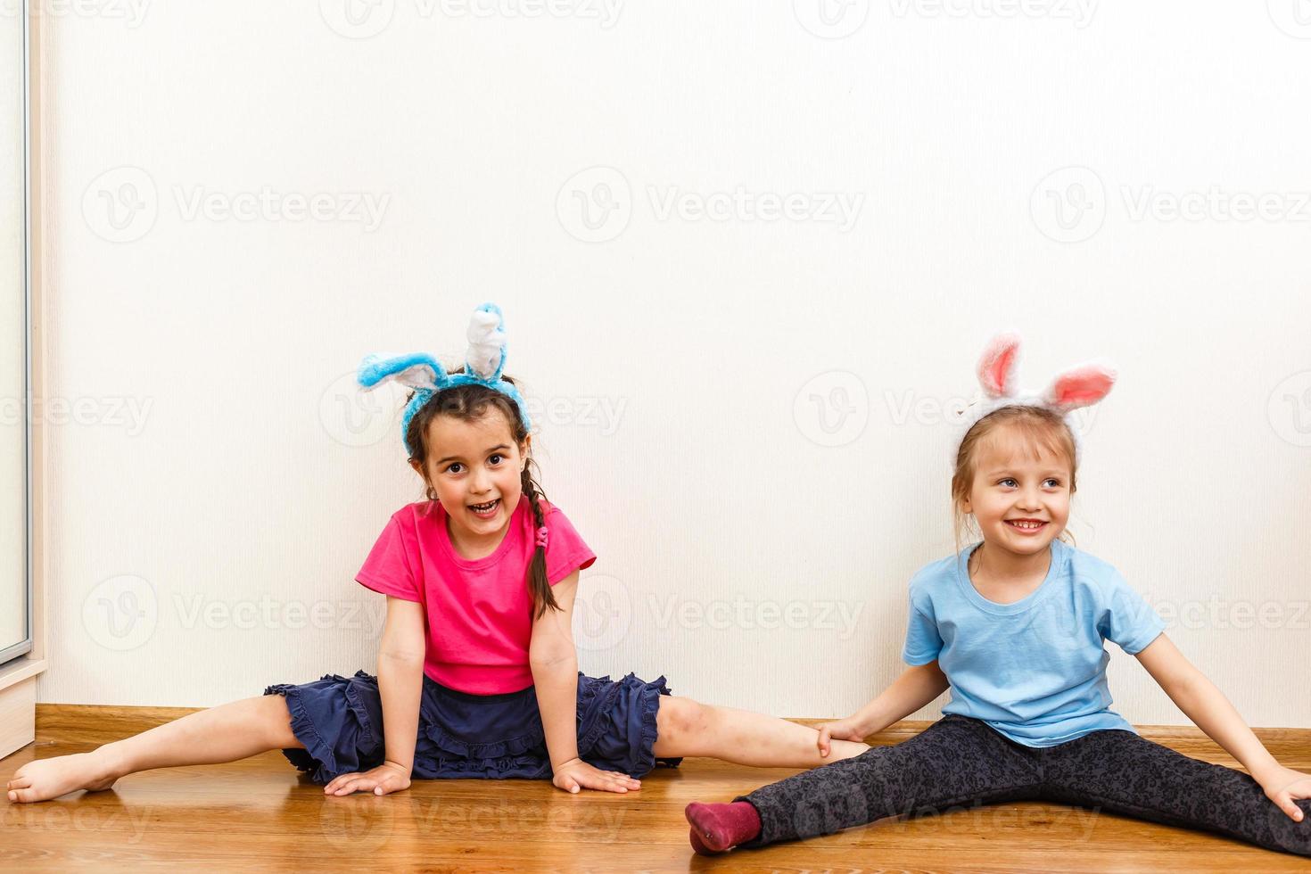 Two smiling girls with rabbit ears holding a box with easter eggs on background. photo