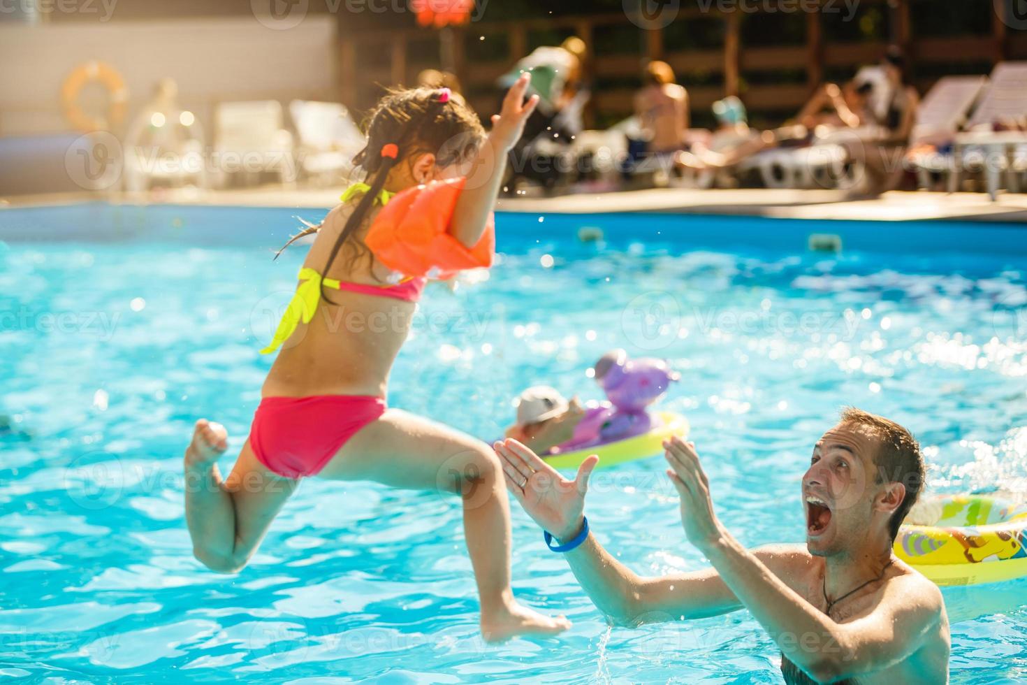 Happy active family young father and his cute daughter adorable toddler girl playing in a swimming pool jumping into the water enjoying summer vacation photo