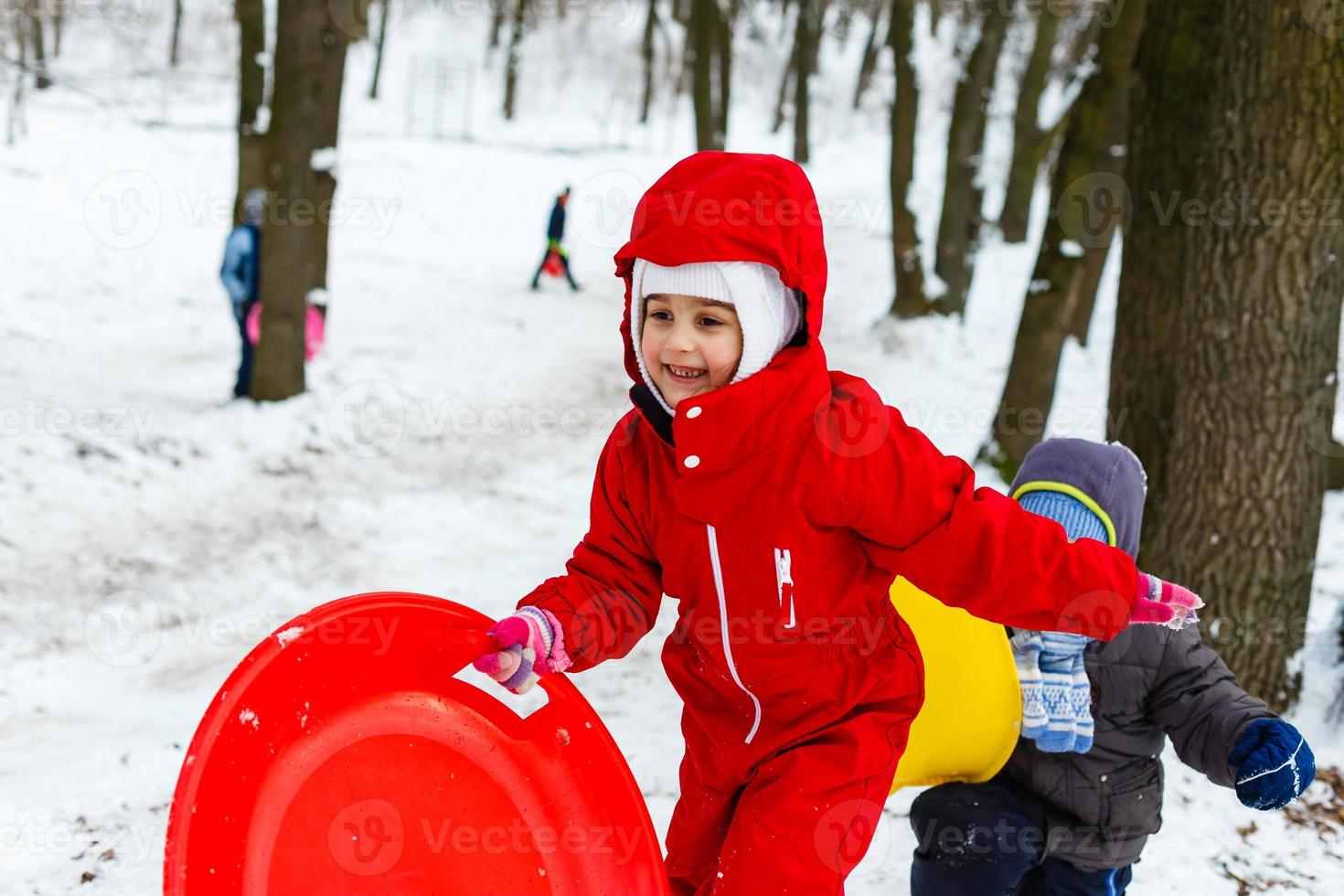 Pretty smiling little girl in her ski suit sliding down a small snow covered hill with her sledge photo