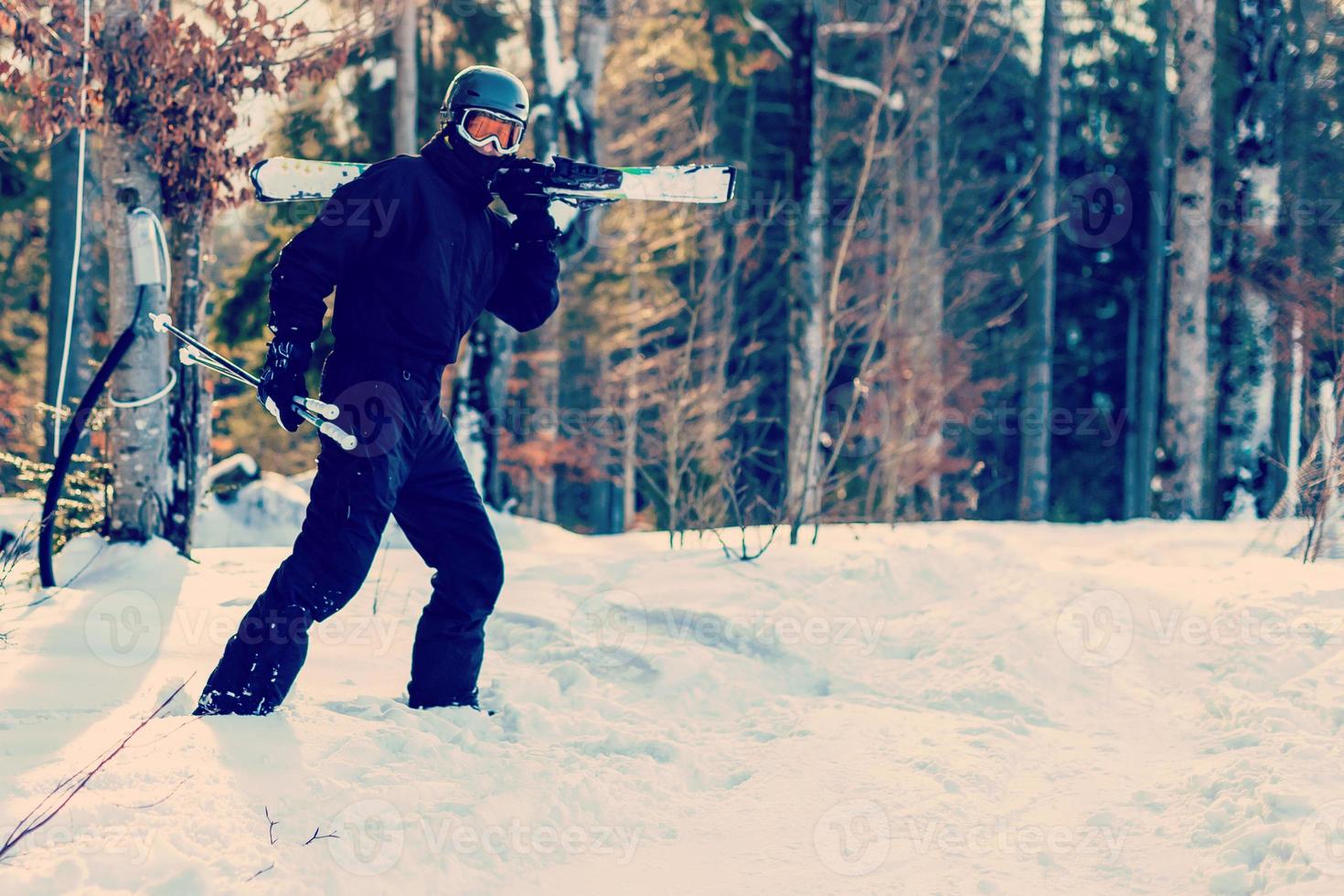 Skier ready holding skiing equipment with sun back light on ski slope - Young athlete in snow mountains for winter vacation - Sport concept and holidays concept - Focus on his face - Warm filter photo