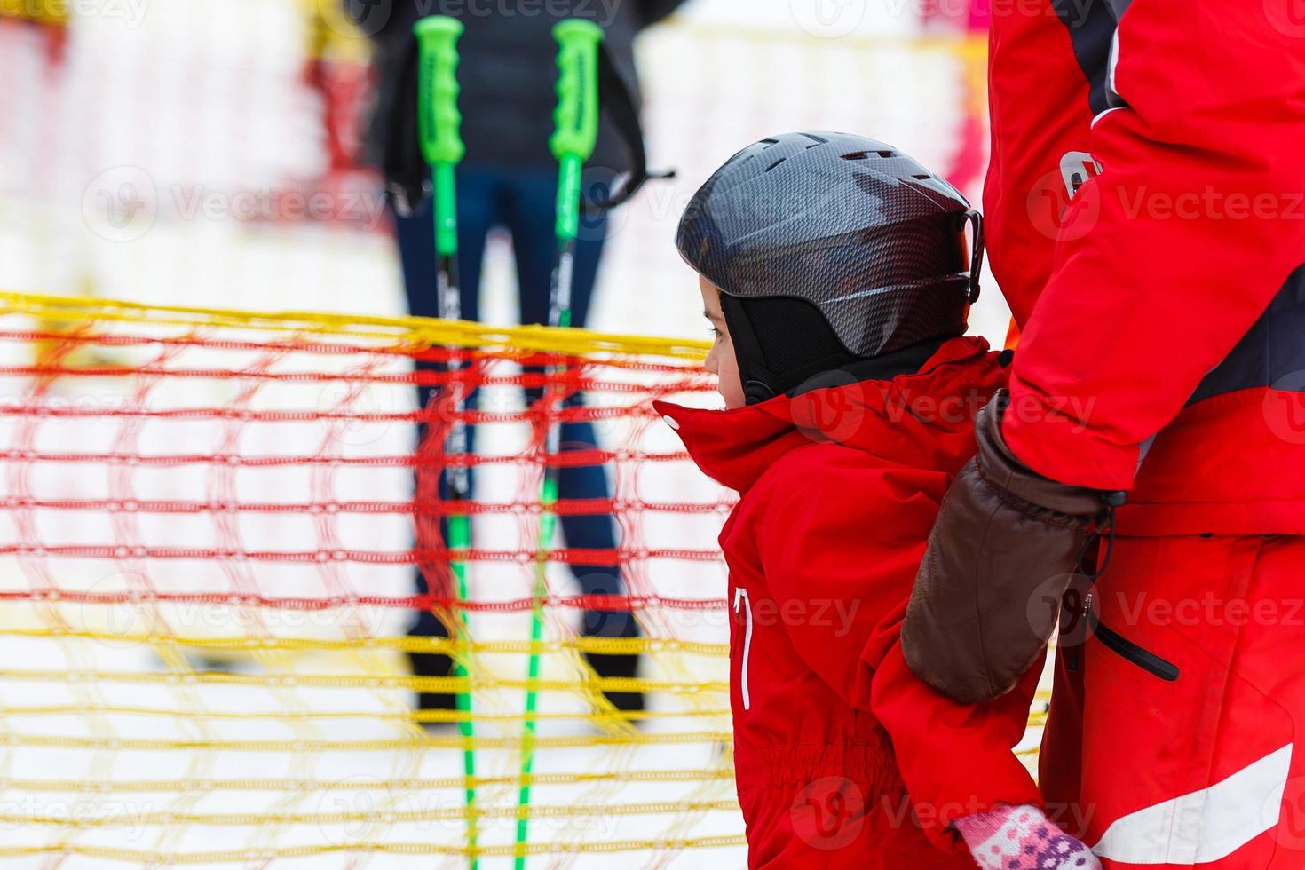 Little girl in red learning to ski with the help of an adult photo